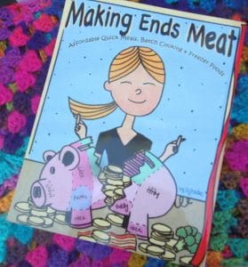 Cover of the cookbook "Making Ends Meat" featuring cartoon woman happily slicing into labeled piggy banks surrounded by stacks of coins, symbolizing budget-friendly bulk cooking, on a colorful crocheted background.